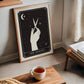 Wood-framed The Stylist art print showing a hand holding scissors, displayed beside a window and tea table.