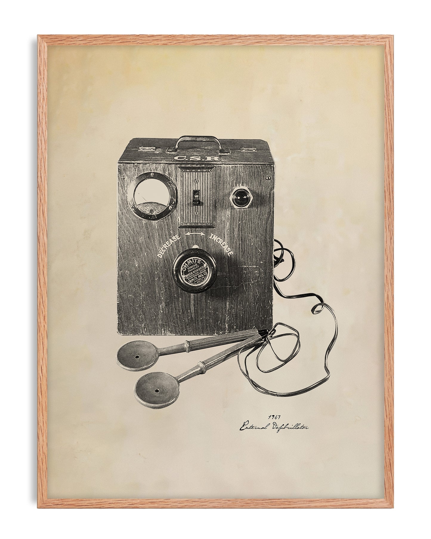Oak-framed art print illustrating a 1947 external defibrillator with a wooden control box and wired paddles.