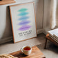 Oak-framed Hierarchy of Needs art print leaning beside a window in a reading area.