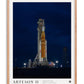 Oak-framed Artemis II art print showing a NASA rocket on an illuminated launch pad at night.