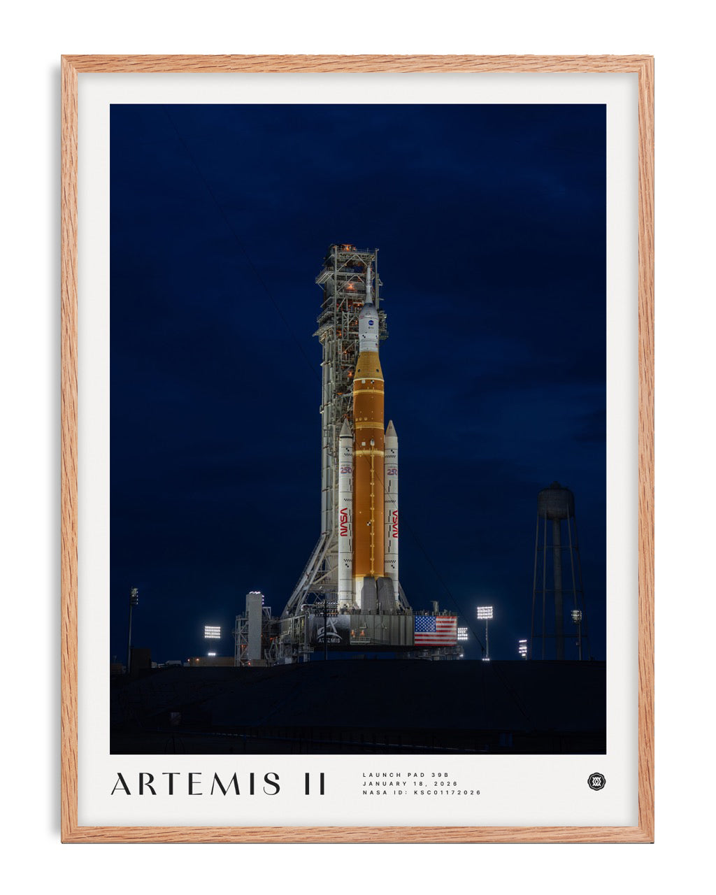 Oak-framed Artemis II art print showing a NASA rocket on an illuminated launch pad at night.