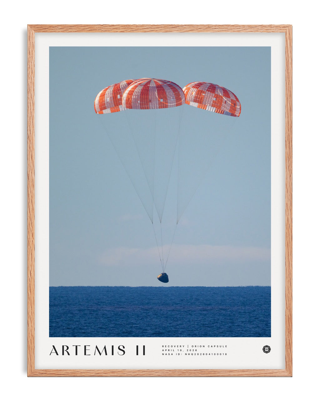 Oak-framed Artemis II art print showing the Orion capsule descending beneath three parachutes over the ocean.
