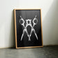 Oak-framed black and white scissors artwork leaning against a wall between two chairs.