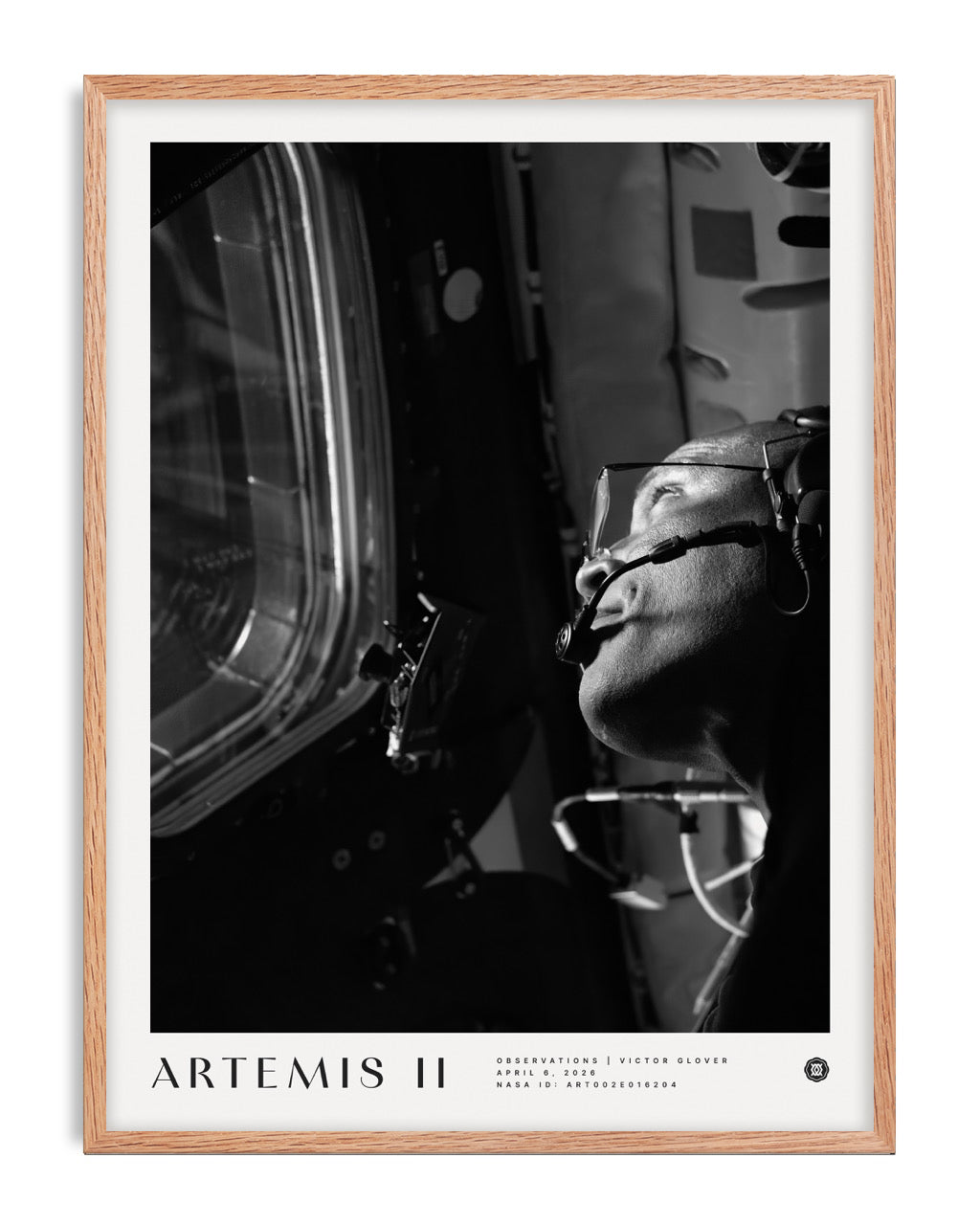 Oak-framed Artemis II art print showing a black-and-white portrait of an astronaut wearing a headset beside a spacecraft window.