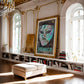 Ornate gold-framed Venice carnival mask artwork displayed above bookshelves in an elegant sunlit room.