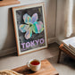 Oak-framed Tokyo 1982 Festival of the Cherry Blossoms artwork leaning near a window in a living room with a cup of tea in front.