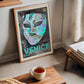 Rose-gold-framed Venice carnival mask artwork leaning beside a window, books, and a cup of tea.