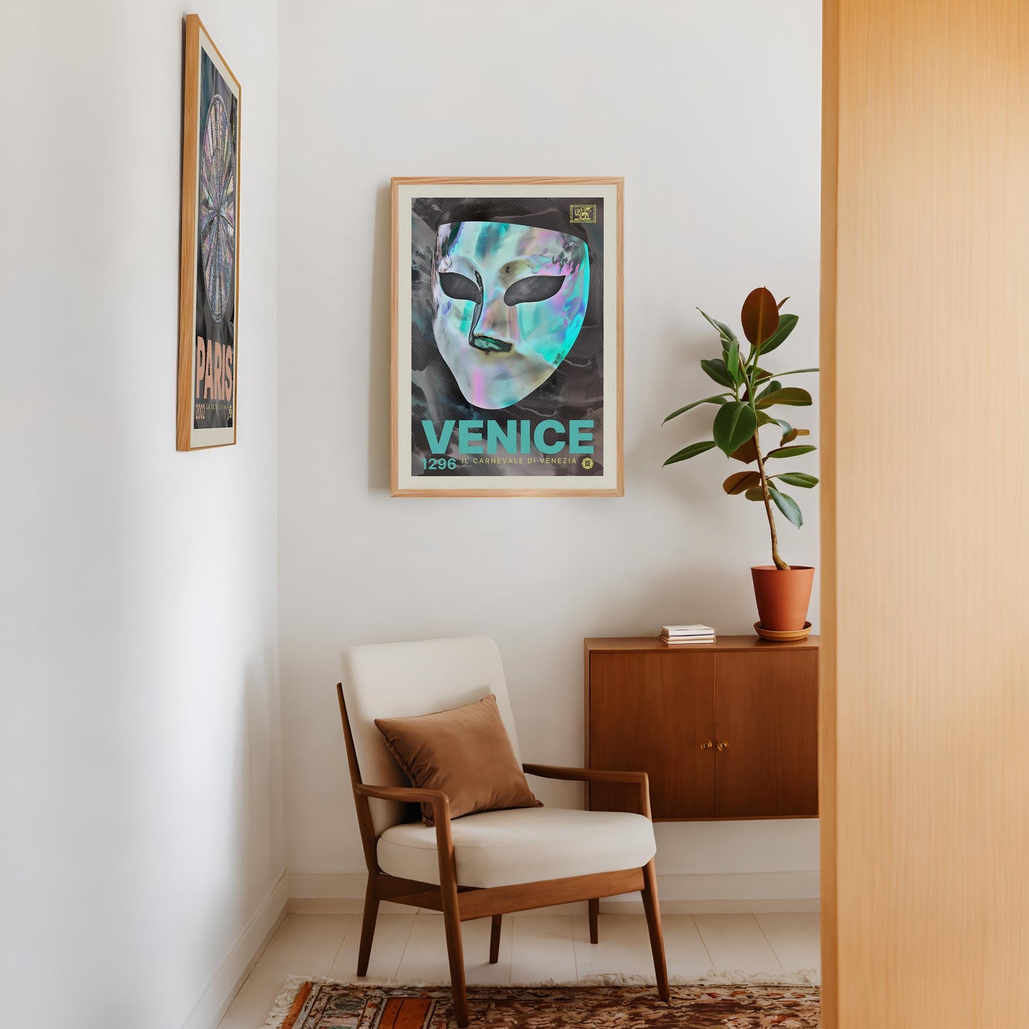 Oak-framed Venice carnival mask artwork displayed above a mid-century armchair beside a potted plant.