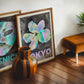 Oak-framed Tokyo 1982 Festival of the Cherry Blossoms artwork leaning with another art print behind a striped wooden vase.