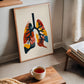 Framed colorful lung anatomy artwork leaning beside a window, books, and a cup of tea.