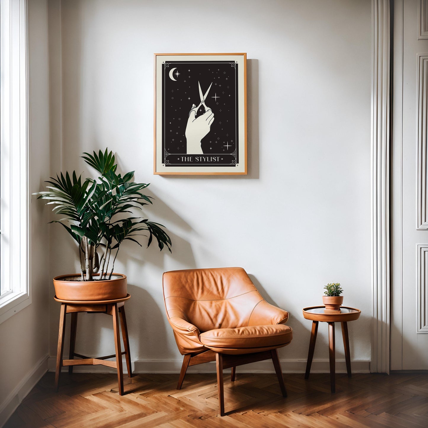 Oak-framed The Stylist art print displayed above a tan leather chair between two potted plants.