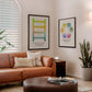 Black-framed Polyvagal Ladder and Feelings Wheel art prints displayed above a tan leather sofa in a living room.