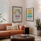 Black-framed Feelings Wheel and Window of Tolerance art prints hanging above a tan leather sofa in a living room.