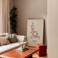 Oak-framed oxytocin molecular artwork leaning beside a cream sofa in a warm-toned living room.