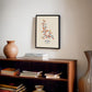 Black-framed oxytocin molecular artwork displayed above a wooden bookcase with books and a ceramic vase.