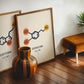 Oak-framed dopamine molecular artwork leaning beside a serotonin print and striped wooden vase in an interior setting.