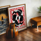 Oak-framed Chōwa artwork with intertwined black-and-white koi fish, leaning beside another art print and a striped wooden vase.