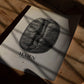 Unframed Yemen Mokha Haraaz art print with a black coffee bean and map outlines lying on a wooden table beneath dramatic shadows.