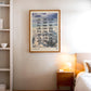 Oak-framed Sky Codes art print with airport abbreviations over painted clouds, displayed above a bedside table in a bedroom.