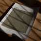 Unframed HIKE. art print with winding map lines and tree symbols lying on a sunlit wooden table.