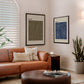 Black-framed HIKE. and RIDE. artworks hanging above a tan leather sofa in a living room.