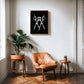 Oak-framed scissors artwork hanging above a tan leather chair between two potted plants.