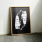 Oak-framed Clippers artwork displayed on the floor between two chairs in an interior setting.