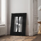 Black-framed white abstract comb artwork leaning against a wall in a bright interior.