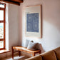 Oak-framed RIDE. bicycle artwork hanging above a wooden bench with cushions in a bright room.