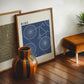 Dark wood-framed RIDE. bicycle artwork leaning beside an olive HIKE. print, striped vase, and tan stool.