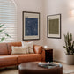 Black-framed RIDE. and HIKE. artworks hanging above a tan leather sofa in a living room.