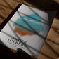 Unframed Anger Iceberg art print lying on a wooden table beneath window shadows.