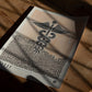Unframed Caduceus art print lying on a wooden floor in patterned sunlight and shadow.