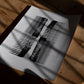 Unframed abstract black-and-white art print with two distressed comb forms on a sunlit wooden table.