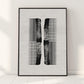Black-framed abstract comb artwork leaning against a light wall on a tiled floor.