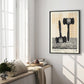Black-framed gavel art print displayed beside tall windows in a bright room with a cushioned window seat, books, and flowers.