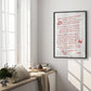 Black-framed art print with red handwritten dining advice displayed beside a bright window and cushioned bench.