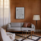 Black-framed handwritten dining advice artwork displayed above a gray sofa on a wood-paneled wall.