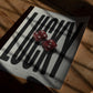 Unframed LUCKY artwork with two red dice lying on a wooden table in patterned sunlight.
