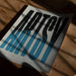 Unframed Artsy art print with elongated black-to-blue letters lying on a wooden table in dappled sunlight.
