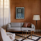 Black-framed Defend typography artwork displayed above a gray sofa in a wood-paneled living room.