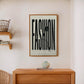 Oak-framed FASHION typography artwork with button and thread displayed above a wooden cabinet.