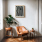 Oak-framed FASHION typography artwork displayed above a tan leather chair and potted plants.