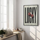 Black-framed LUCKY art print with two glossy red dice displayed beside a sunlit window seat.