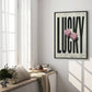 Black-framed LUCKY art print with two pink fuzzy dice displayed beside a sunlit window seat.