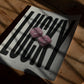 Unframed LUCKY art print with two pink fuzzy dice lying on a wooden table in dappled sunlight.