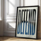 Black-framed Defend typography artwork with black-to-blue elongated letters, leaning against a sunlit paneled wall.