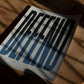 Unframed Defend art print with elongated black-to-blue letters lying on a wooden table in dappled sunlight.