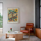 Black-framed Hepar in Bloom artwork displayed beside a rust-colored armchair in a modern sitting room.