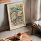 Copper-toned framed Hepar in Bloom artwork leaning near a window beside books and a cup of tea.